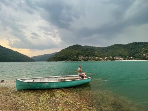 A view of a sea and mountains and a male standing on the boat in Bosnia and Herzegovina