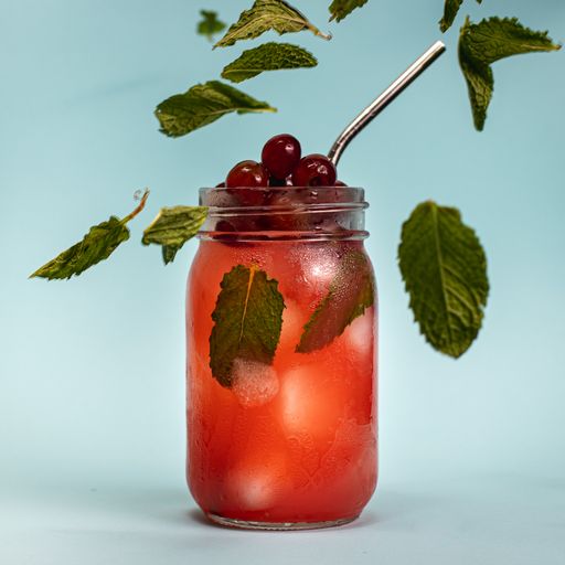 A glass jar of drinks with tart cherries and mint leaves isolated on blue background