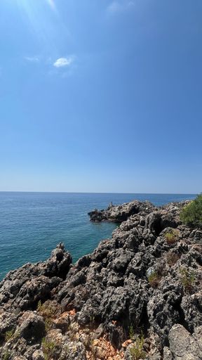 Rocky coastline under a clear blue sky with calm sea, perfect for nature and travel themes.