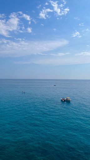 A serene seascape with small boats floating on clear blue water under a partly cloudy sky, capturing a peaceful maritime scene.