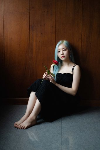 A beautiful blue-haired South Korean female with a single red rose sitting on a floor