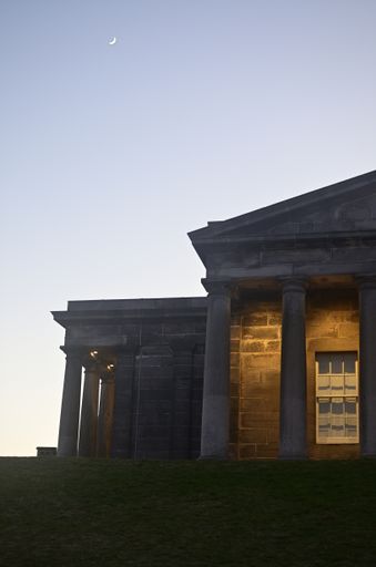 A vertical shot of a Roman-style building with a visible crescent moon in a clear sky