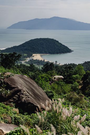 Scenic view of lush green hills and a sandy beach with distant mountains under a partly cloudy sky.