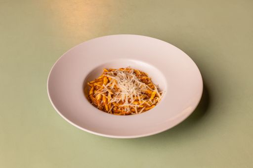 A plate of pasta with tomato sauce and grated cheese on a light green table.