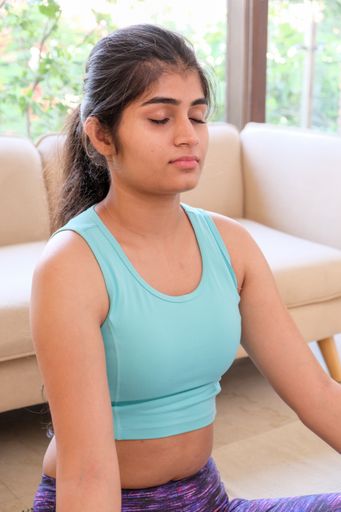 A young Indian female in sportswear practicing yoga at home