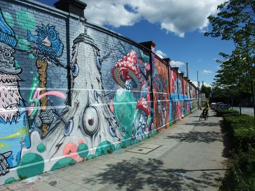 Vibrant street art on a long wall with a cyclist passing by under a blue sky, showcasing urban creativity and colorful graffiti.
