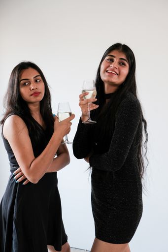 A vertical closeup of two girls in black dresses with glasses of champagne.