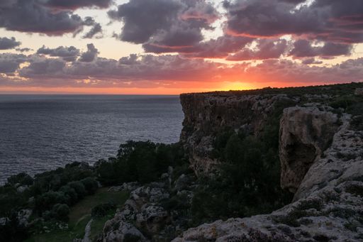 Reddish sky and clouds during a peaceful beautiful sunset as seen from the high limestone cliffs along the northern coast of Mellieha, Malta.