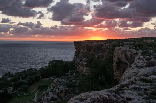 Reddish sky and clouds during a peaceful beautiful sunset as seen from the high limestone cliffs along the northern coast of Mellieha, Malta.