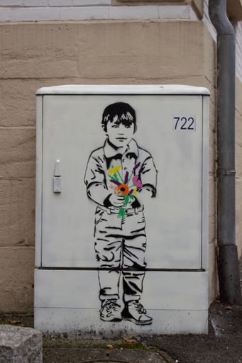 A vertical shot of a street art of a young boy holding colorful flowers on an urban utility box, blending creativity and urban environment