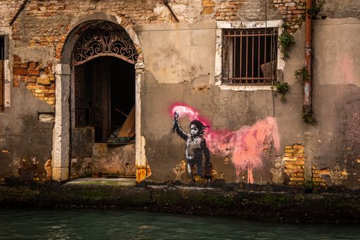 Street art of a child holding a flare on an old Venetian building wall, with vibrant pink paint, reflecting urban creativity and cultural expression.