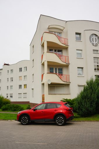 A parked red car in front of a four-floor high apartment building in the Stare Zegrze district.