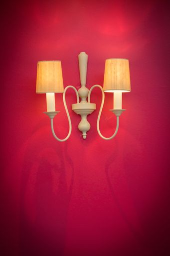 A vertical shot of illuminated vintage sconces on a red wall