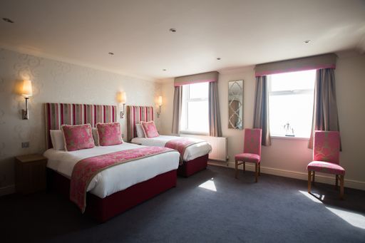 A simple hotel bedroom interior with single and double-sized beds, red cushions and chairs