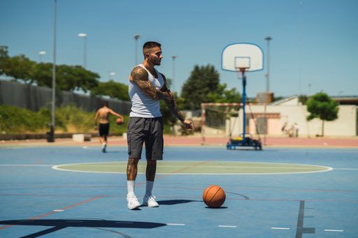 A young caucasian guy with cool tattoos standing on the basketball court with a ball