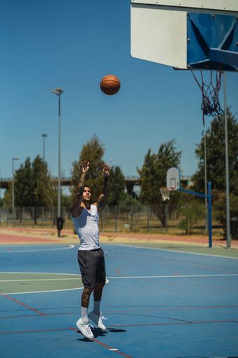 A vertical shot of a caucasian guy with cool tattoos throwing the basketball ball to the hoop