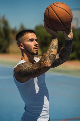 A handsome caucasian basketball player with cool tattoos standing on the court throwing the ball up