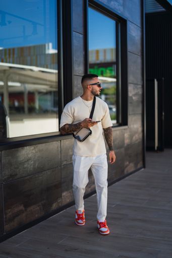 A cool caucasian guy with sunglasses and tattoos standing on the background of a building with a phone