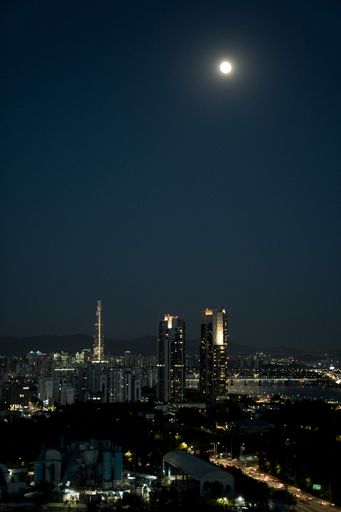A vertical shot of an illuminated night cityscape under the full moon in South Korea