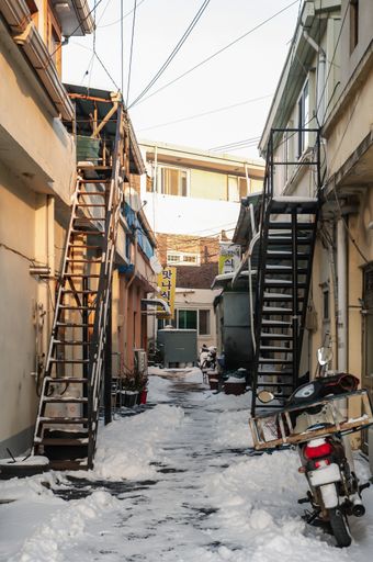 A snowy little roadway that goes through old buildings with staircases in South Korea