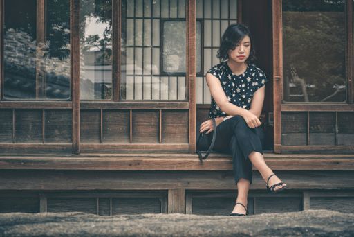 A sad East Asian girl sitting on a wooden doorway and waiting for someone