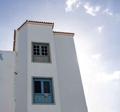 A minimalist view of a white building with blue windows against a bright sky, capturing architectural simplicity.