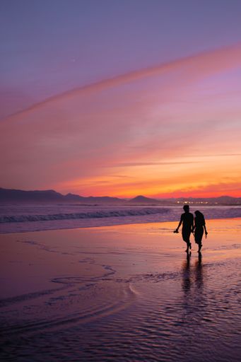 A silhouette shot of a sweet couple walking on the seashore during sunset in South Korea