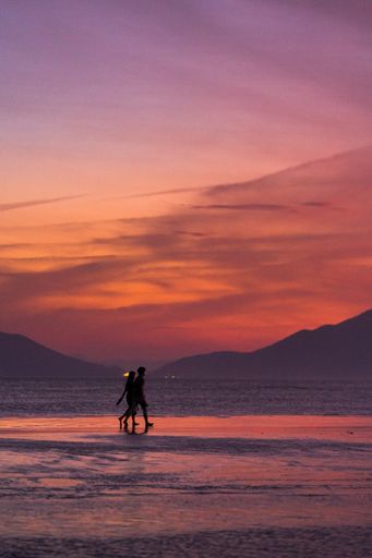 A vertical shot of a couple walking along the beach during sunset