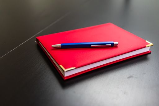 A closeup shot of a red notebook with a blue pen on a table