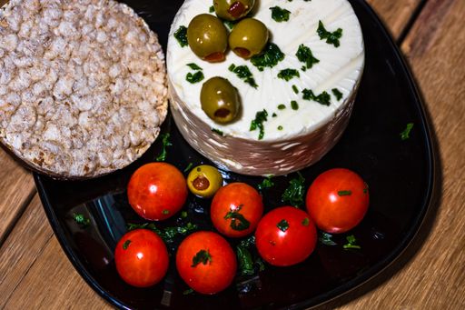 A high angle shot of tasty white cheese with spices, olives and cherry tomatoes on a cutting board