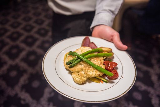A closeup of a waiter showing a plate of steak slices with vegetables and asparagus in a restaurant