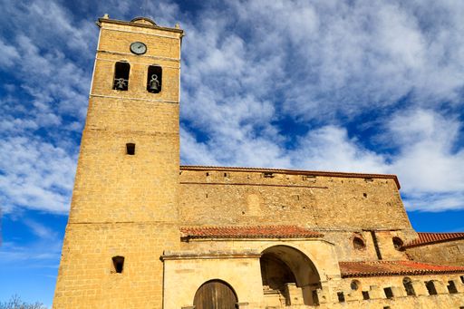Historic stone bell tower under a vibrant blue sky with scattered clouds, showcasing architectural beauty.