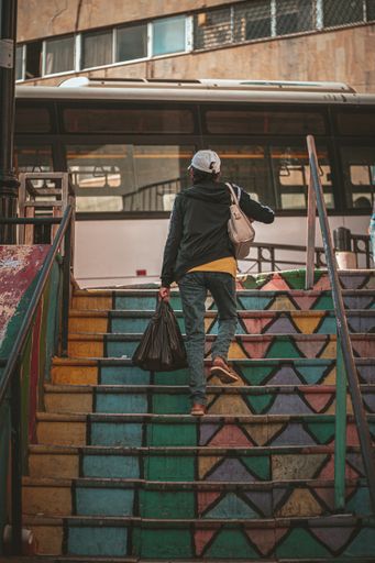 A vertical shot of a person holding a plastic bag and climbing up the colorful stairs on a sunny day