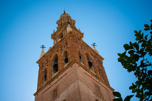 Low angle view of a historic brick tower against a clear blue sky, framed by leafy branches, showcasing architectural details.