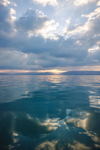 A tranquil seascape with serene waters reflecting a dramatic cloudy sky at sunset.