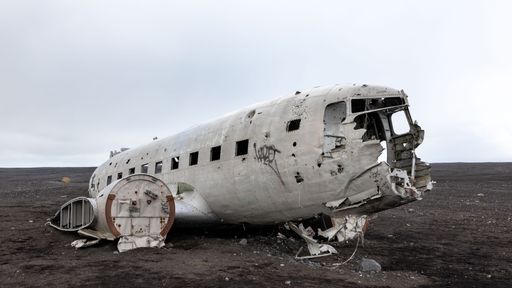 Abandoned airplane wreckage on a desolate black sand beach in Iceland, under a cloudy sky.