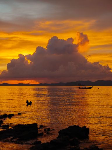 A scenic sunset over a tranquil sea with a silhouetted boat and dramatic clouds. Krabi, Thailand