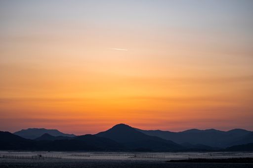A high angle shot of a landscape with a mountain silhouette and a golden skyline after sunset