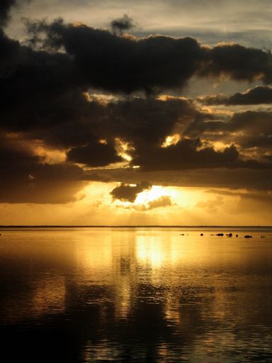 A vertical shot of a sea under a cloudy sky with the sun shining behind the clouds in Tahiti. Bora  Bora
