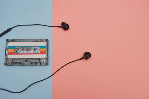 A colorful music cassette and headphones on light blue and light brown background