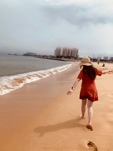 A vertical shot of a beautiful girl in a red dress walking on the beach