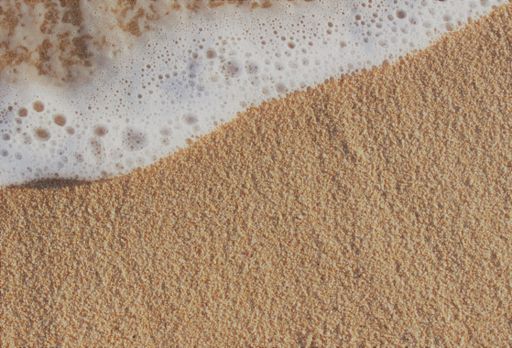Close-up overhead view of the edge of white ocean water on clean golden beach sand