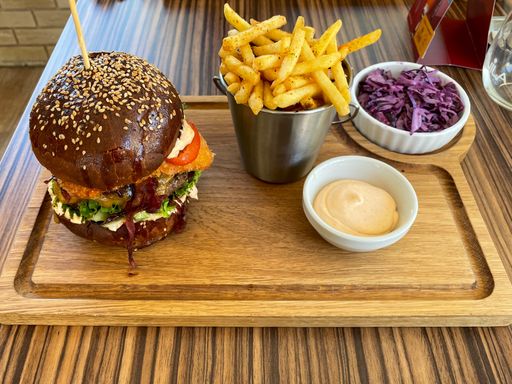 A shot of a delicious burger, french fries, stewed red cabbage, and sauce served on a wooden tray