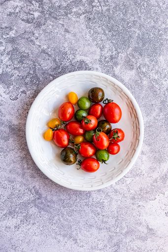 Multi coloured baby tomatoes in ceramic bowl on marble surface
