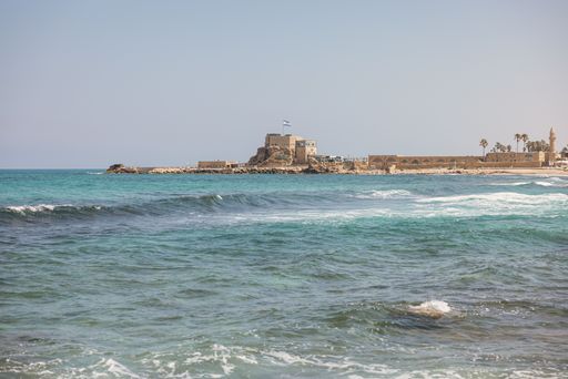 A scenic view of the Mediterranean Sea with ancient ruins and palm trees in Caesarea, Israel