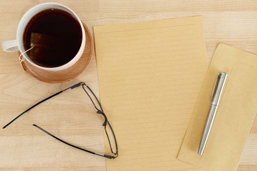 A top view of a blank letter paper, envelope, and a teacup, on a wooden office desk