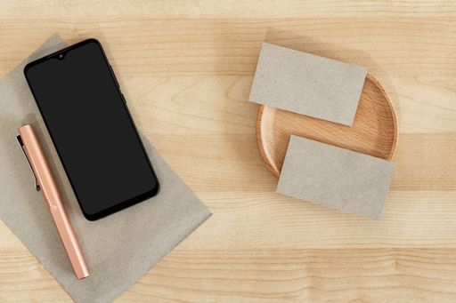 A top view of blank business cards and a smartphone on a wooden office table, recycled paper
