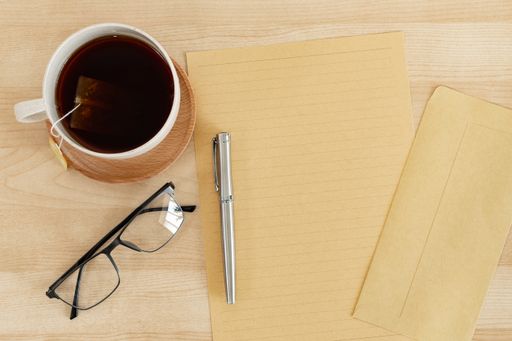 A top view of a blank letter paper, envelope, and a teacup, on a wooden office desk