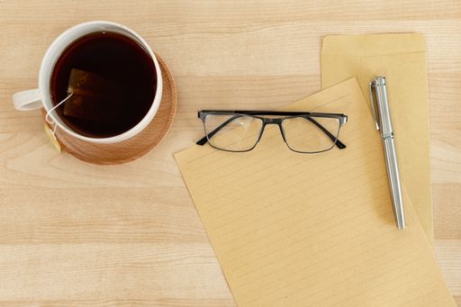 A top view of a blank letter paper, envelope, and a teacup, on a wooden office desk
