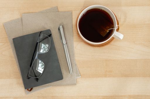 A top view of a notebook, recycled paper, pen, and teacup on a wooden desk